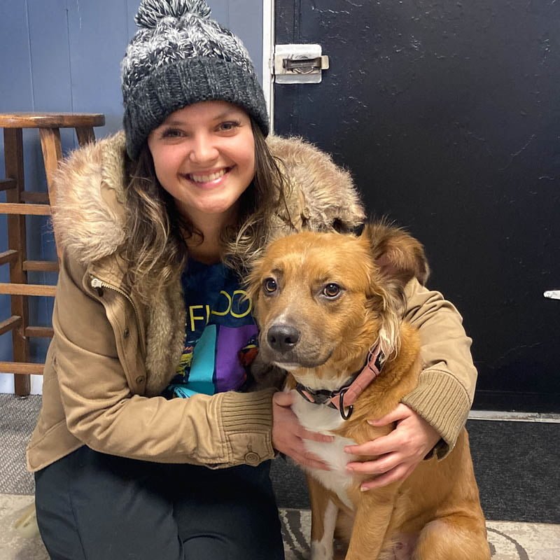 A woman with a winter cap and coat on posing for photo with her dog.